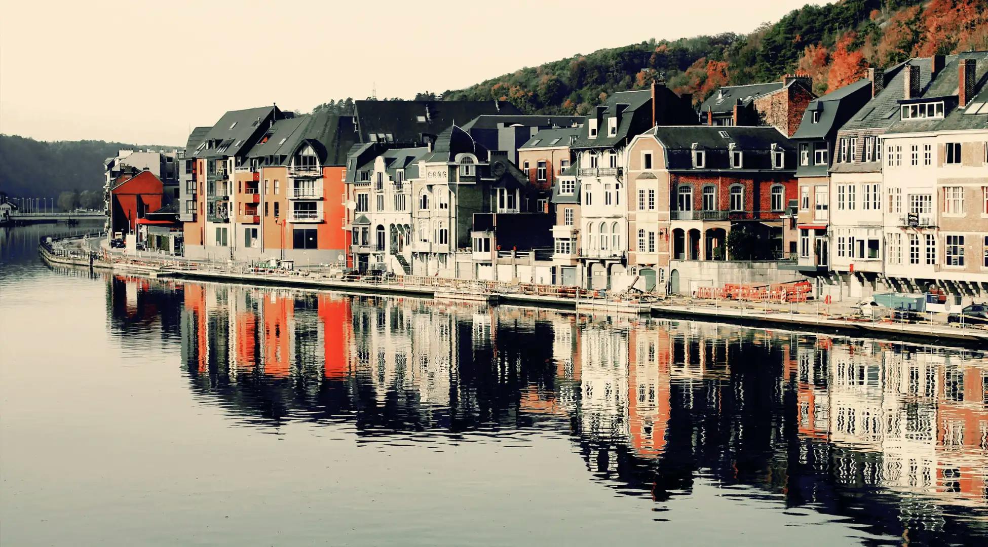 Vue pittoresque des façades colorées se reflétant sur la Meuse à Dinant, une expérience emblématique des escapades Pop'in en Belgique.