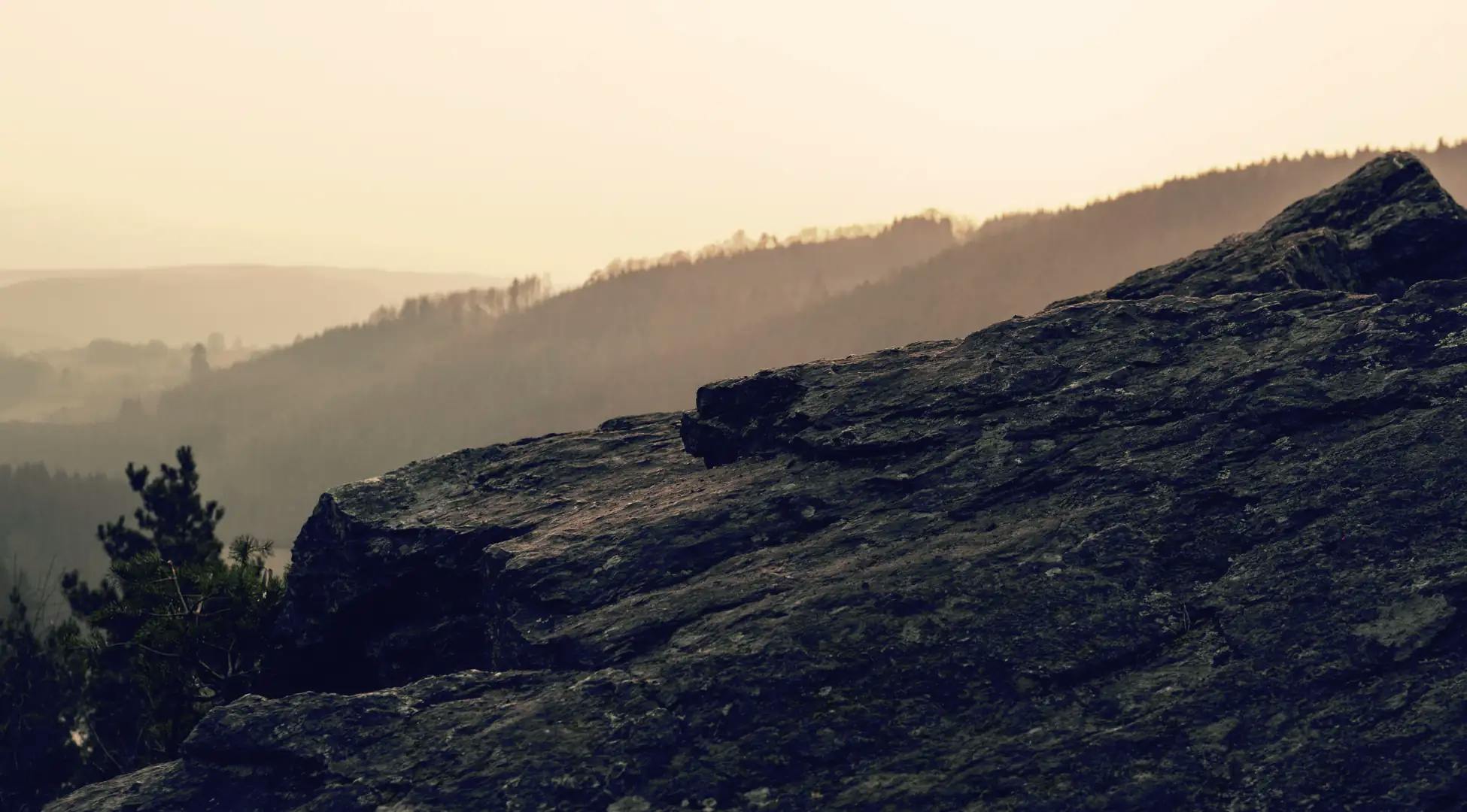 Vue depuis le sommet rocheux au crépuscule avec des forêts brumeuses en arrière-plan, capturant l'essence des randonnées en pleine nature avec Pop'in.